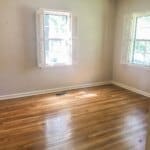 A bright, empty room with two windows, white walls, and polished hardwood floor.